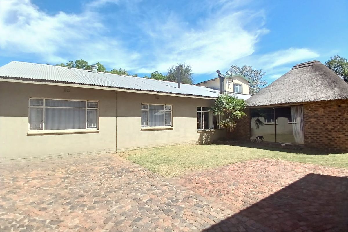 Rear view of the property featuring a paved courtyard, lawn area, and a combination of plastered brick and thatched roof structures.