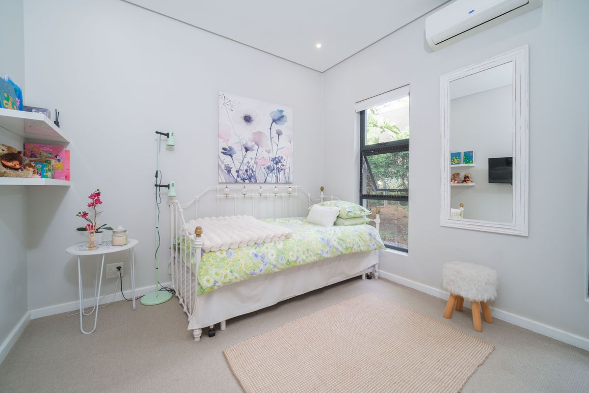 A bright and well-maintained bedroom featuring neutral carpeting, a wall-mounted air conditioning unit, and a large window providing natural light.