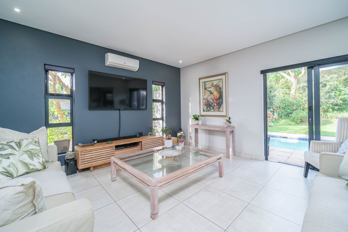 A bright living room featuring large format floor tiles, a feature wall, split-system air conditioning, and sliding glass doors opening to the pool area.