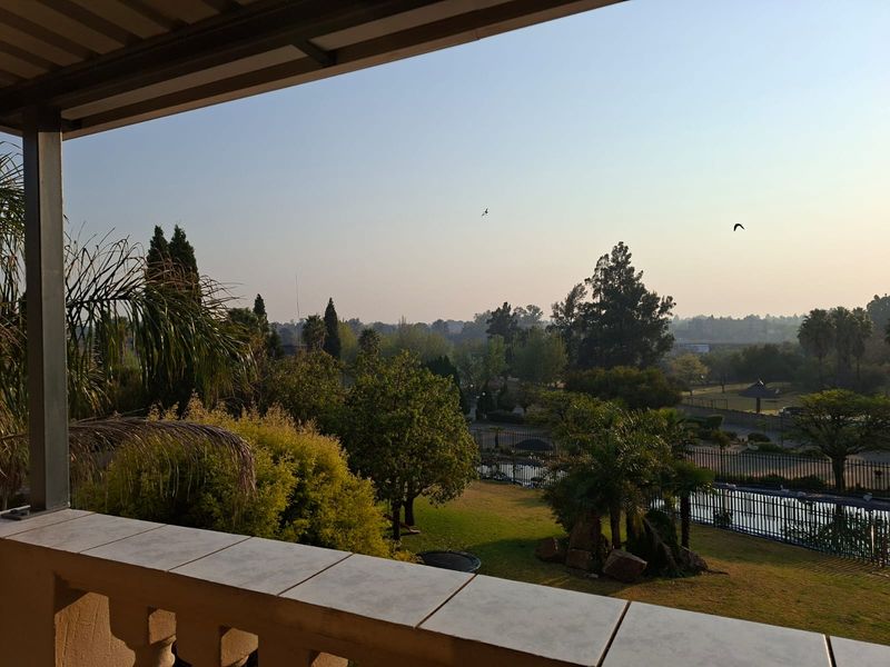 A scenic elevated view overlooking a landscaped garden and pool area from a covered balcony with a tiled railing.