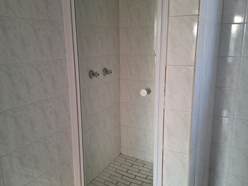 A functional bathroom shower enclosure featuring white wall tiles, a glass door, and tiled flooring.