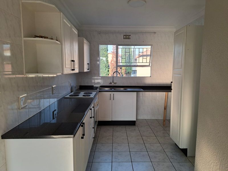 A functional kitchen featuring white cabinetry, dark countertops, tiled splashbacks, and an electric hob, offering a clean canvas for potential updates.