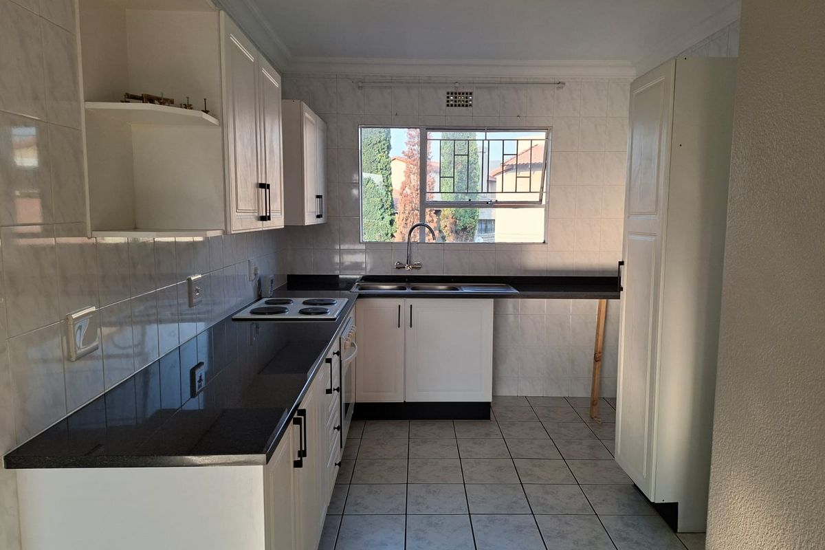 A functional kitchen featuring white cabinetry, dark countertops, tiled splashbacks, and an electric hob, offering a clean canvas for potential updates.