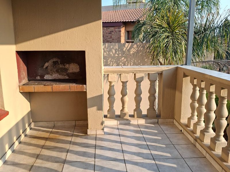 A covered balcony featuring tiled flooring, a built-in braai, and a classic balustrade, offering a functional outdoor entertainment space.