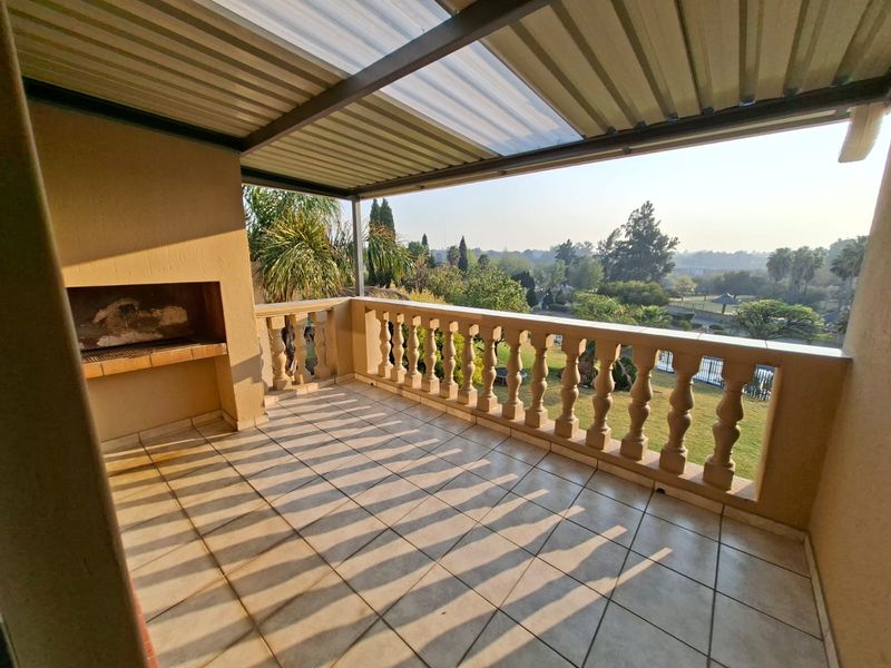 Spacious covered balcony featuring a built-in braai, tiled flooring, and a classic balustrade, offering scenic views of the surrounding garden area.