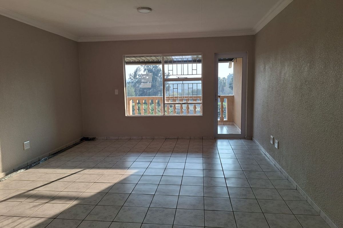 A spacious, empty living area featuring neutral tiled flooring, coved ceilings, and direct access to a balcony through a glass door.
