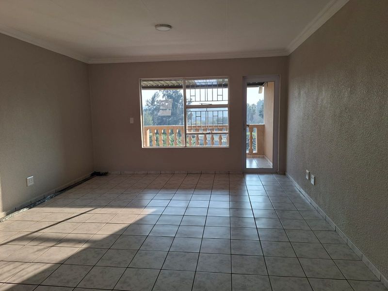 A spacious, empty living area featuring neutral tiled flooring, coved ceilings, and direct access to a balcony through a glass door.