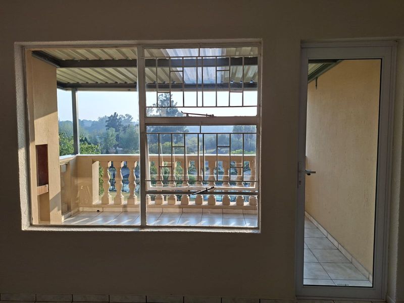 A covered balcony featuring tiled flooring, a decorative balustrade, and security bars, offering an outdoor space accessible through a glass door.