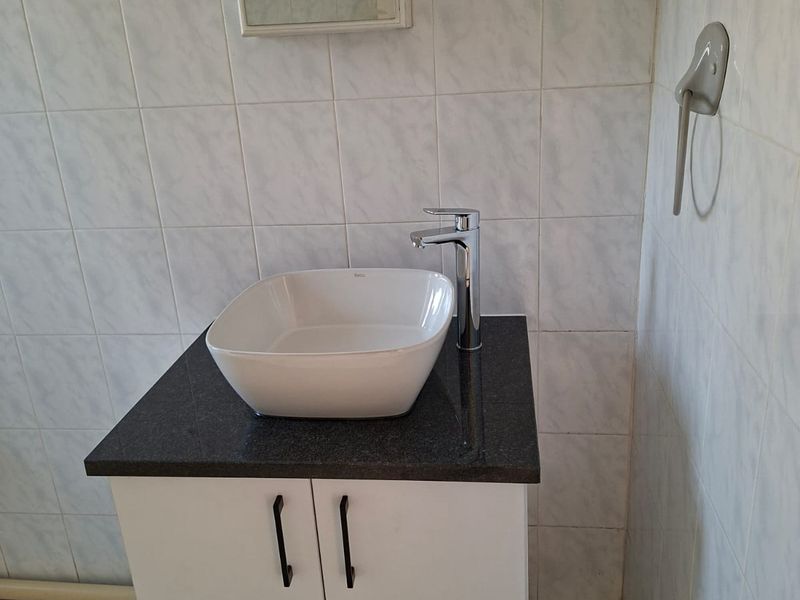 A clean bathroom vanity area featuring a modern vessel sink, granite countertop, white cabinetry, and wall-mounted mirror cabinet with tiled finishes.