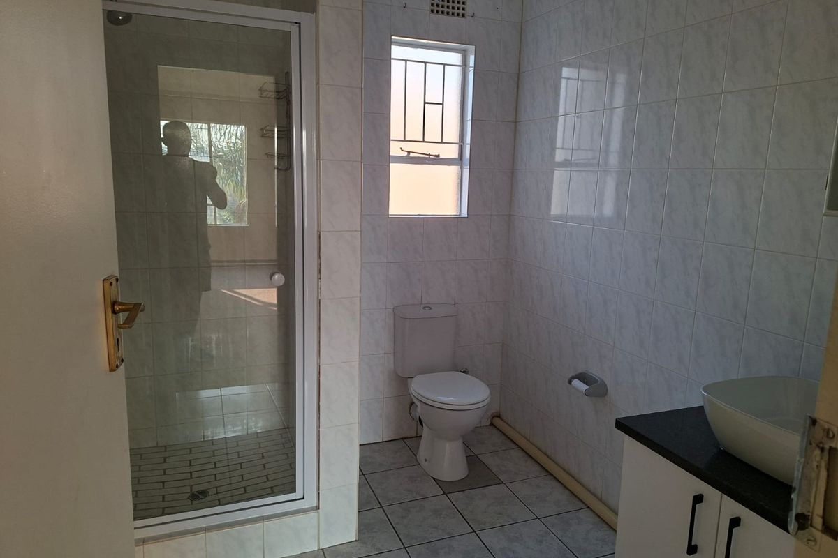 A functional bathroom featuring a glass shower enclosure, a toilet, and a vanity cabinet with a vessel sink, finished with neutral wall and floor tiles.