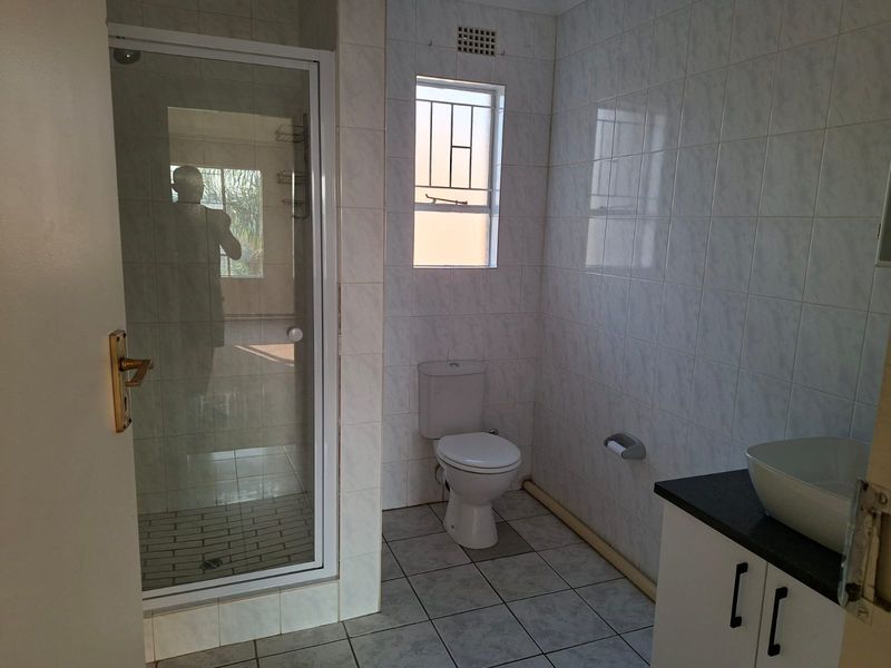 A functional bathroom featuring a glass shower enclosure, a toilet, and a vanity cabinet with a vessel sink, finished with neutral wall and floor tiles.