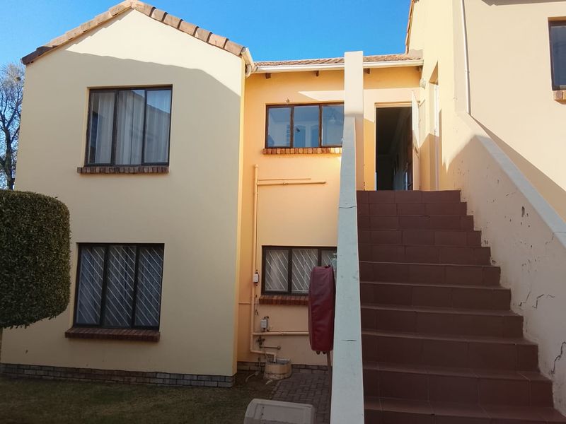 Exterior view of a two-story flat featuring a tiled staircase with a concrete balustrade and aluminium window frames with security bars.