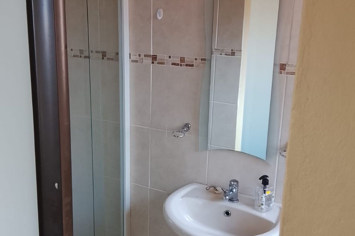 A compact bathroom featuring a pedestal basin, a glass shower enclosure, and neutral wall tiling.