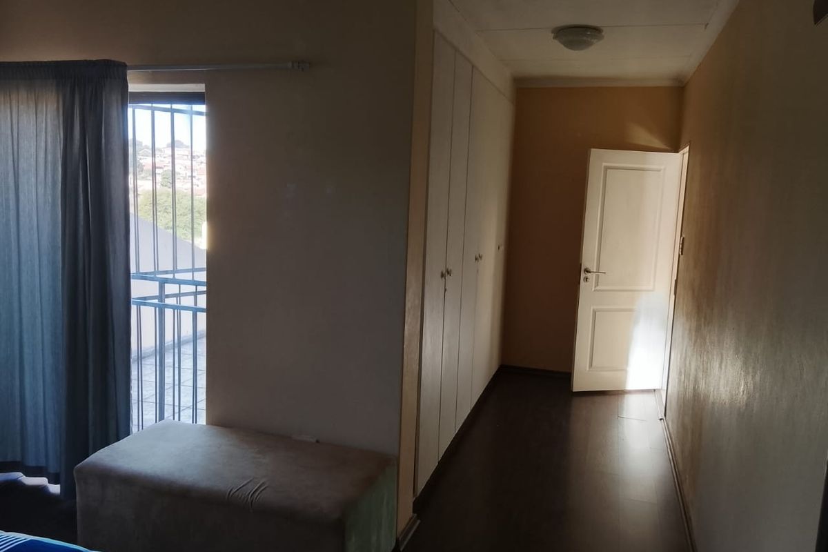 Bedroom featuring built-in cupboards, laminate flooring, and direct access to a balcony through a security gate.