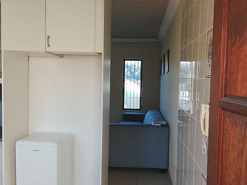 A compact kitchen area featuring tiled walls and flooring, built-in cabinetry, and an intercom system, leading into an adjacent living space.