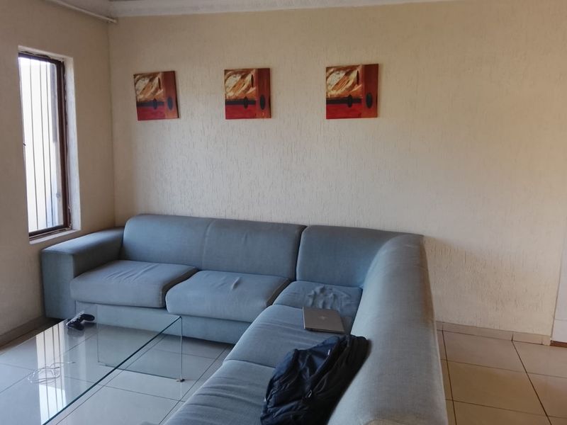 A living room area featuring tiled flooring and a window fitted with security bars, providing a functional and neutral living space.