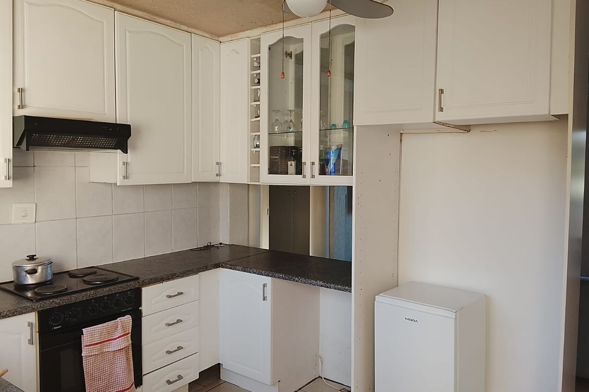 A functional kitchen featuring white built-in cabinetry, dark laminate countertops, an integrated oven and hob, and tiled flooring.