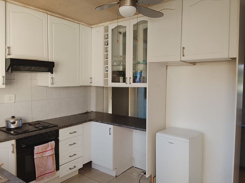 A functional kitchen featuring white built-in cabinetry, dark laminate countertops, an integrated oven and hob, and tiled flooring.