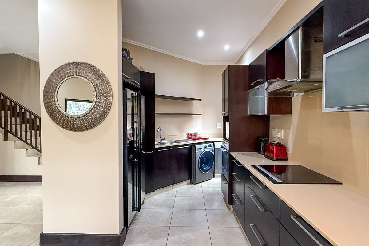 Modern kitchen featuring dark cabinetry, stone countertops, integrated stainless steel appliances, and tiled flooring, with an adjacent staircase visible in the background.