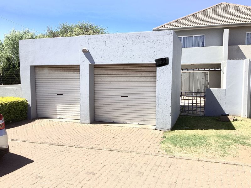 Exterior view of a townhouse featuring a double garage with roller doors and a paved driveway entrance.