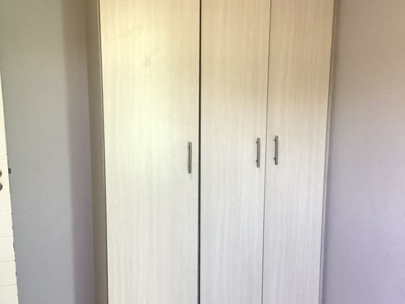 A bedroom featuring a light wood-finish built-in wardrobe and neutral tiled flooring.