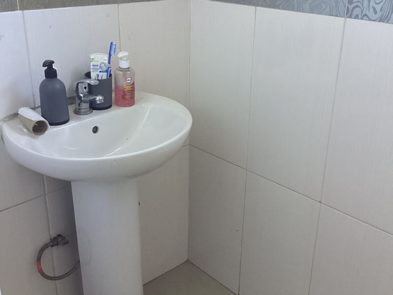 A functional bathroom corner featuring a white pedestal basin with a chrome mixer tap and decorative patterned wall tiling.