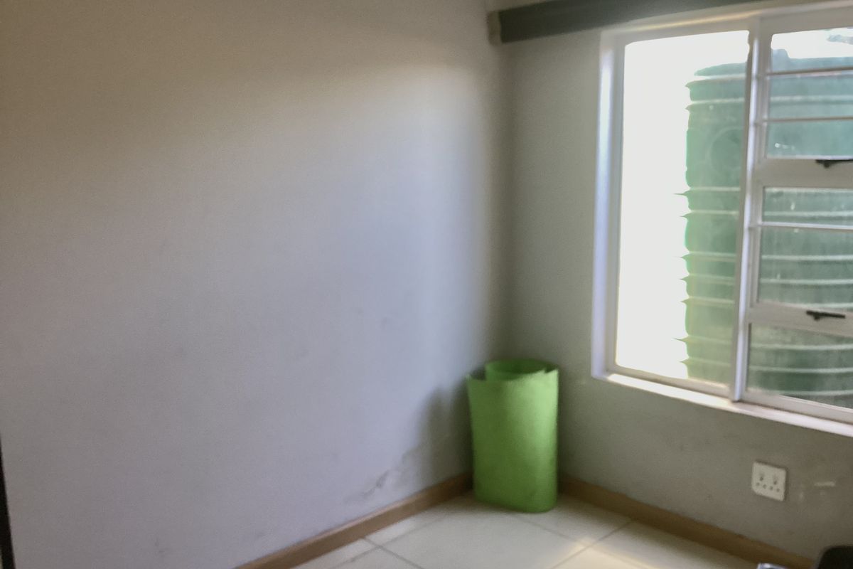 An empty bedroom featuring tiled flooring and a window with an aluminium frame, requiring minor cosmetic updates to the walls.
