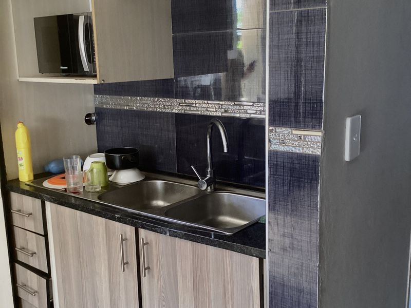 Compact kitchen area featuring modern laminate cabinetry, granite countertops, a double bowl stainless steel sink, and decorative tiled backsplash.