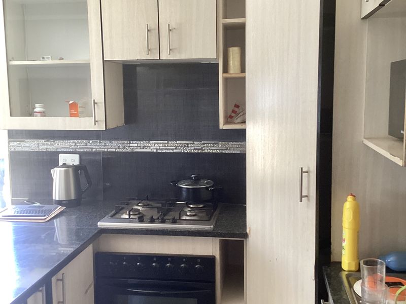 Compact kitchen featuring light wood-finish cabinetry, granite countertops, a gas hob, and a built-in oven with a tiled backsplash.