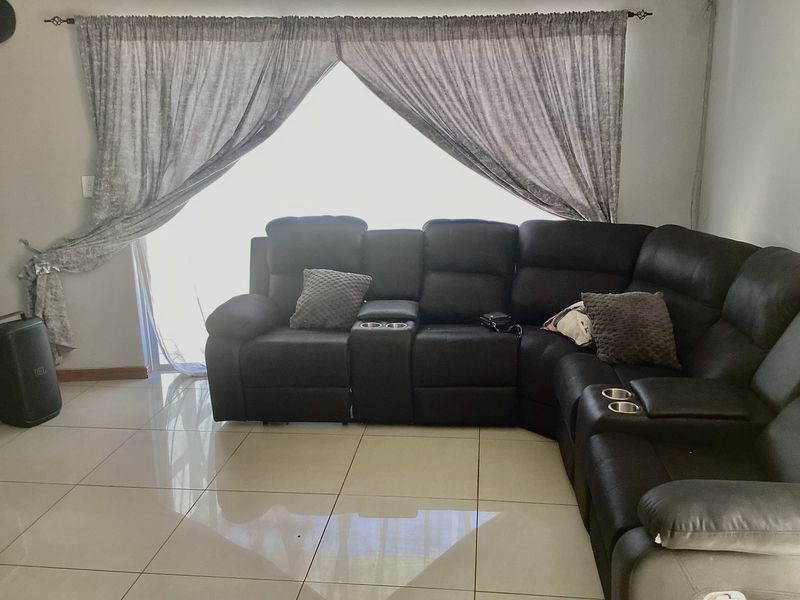 A living room featuring large format floor tiles and a sliding glass door with curtain treatments, providing access to the exterior.