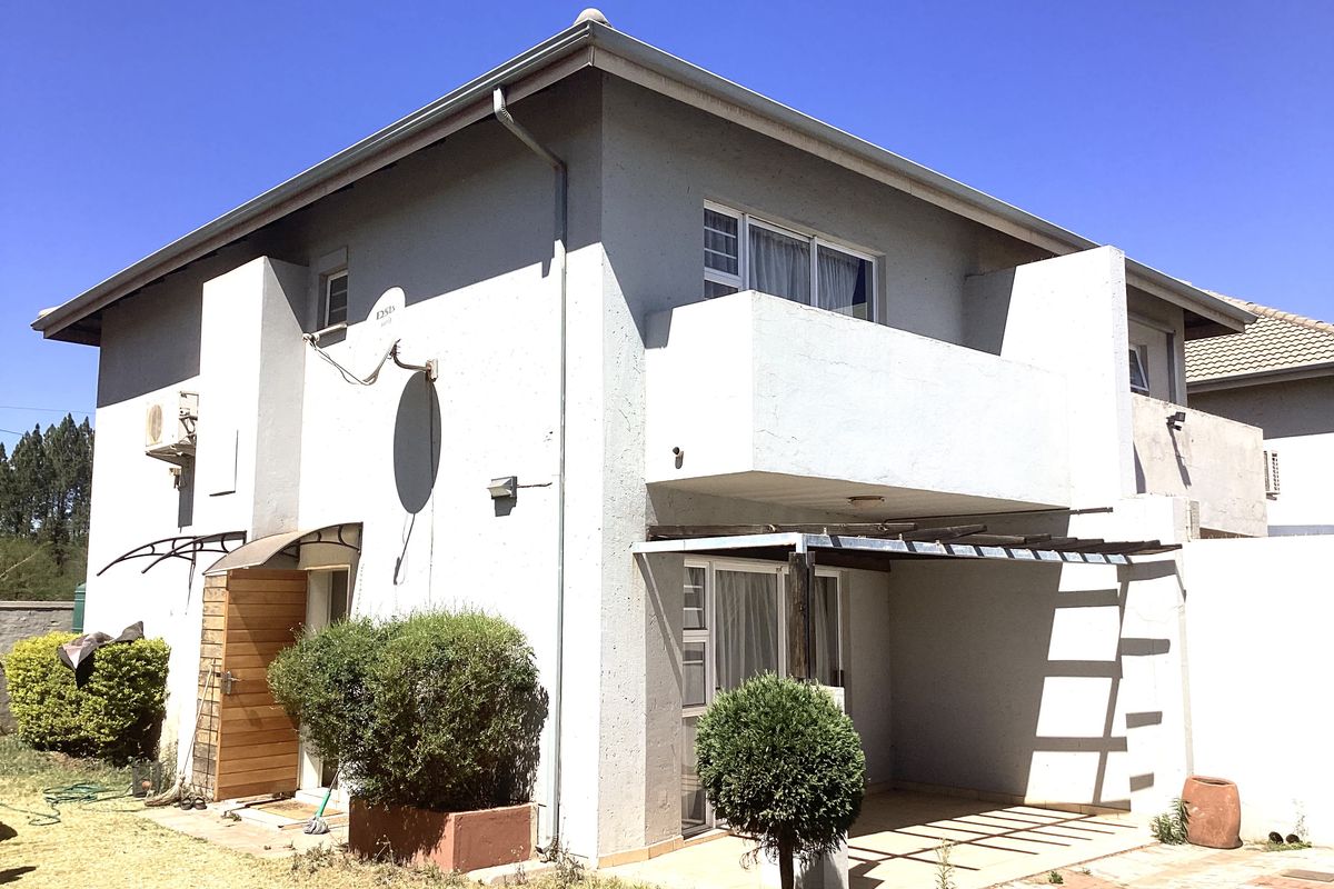 Rear view of a two-story townhouse featuring a covered patio, a first-floor balcony, and a paved outdoor area.