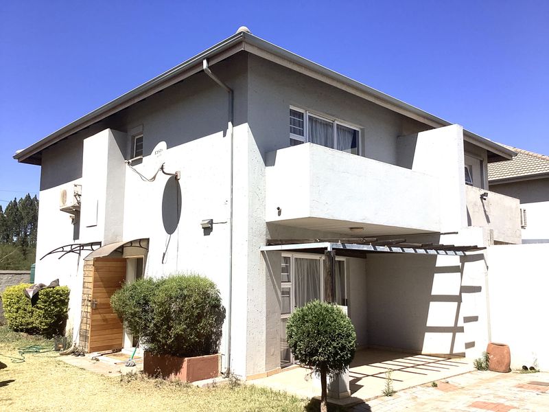Rear view of a two-story townhouse featuring a covered patio, a first-floor balcony, and a paved outdoor area.