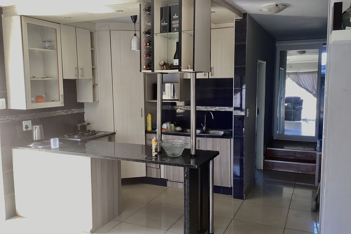 A functional kitchen featuring granite countertops, built-in cabinetry, a gas hob, and tiled flooring, with an open-plan layout leading to an adjacent living area.