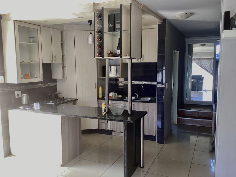A functional kitchen featuring granite countertops, built-in cabinetry, a gas hob, and tiled flooring, with an open-plan layout leading to an adjacent living area.