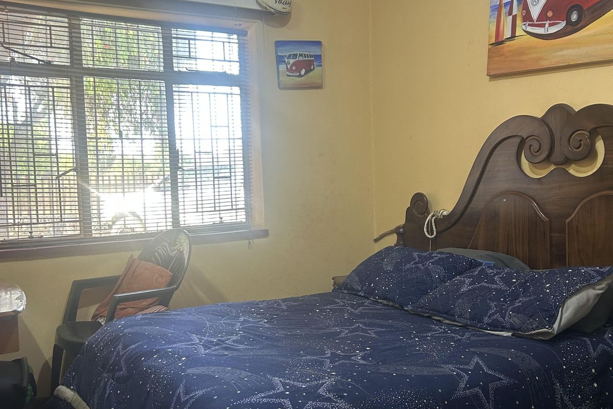 A bedroom featuring carpet flooring, security bars on the window, and decorative cornice, currently showing signs of wear on the walls and ceiling.