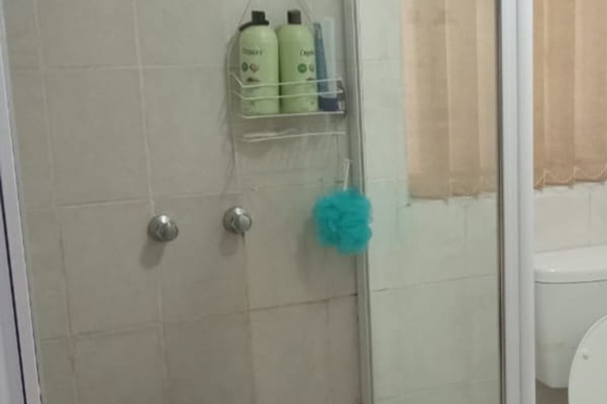 A functional bathroom featuring a glass-enclosed shower with tiled walls and flooring, alongside a standard toilet fixture.