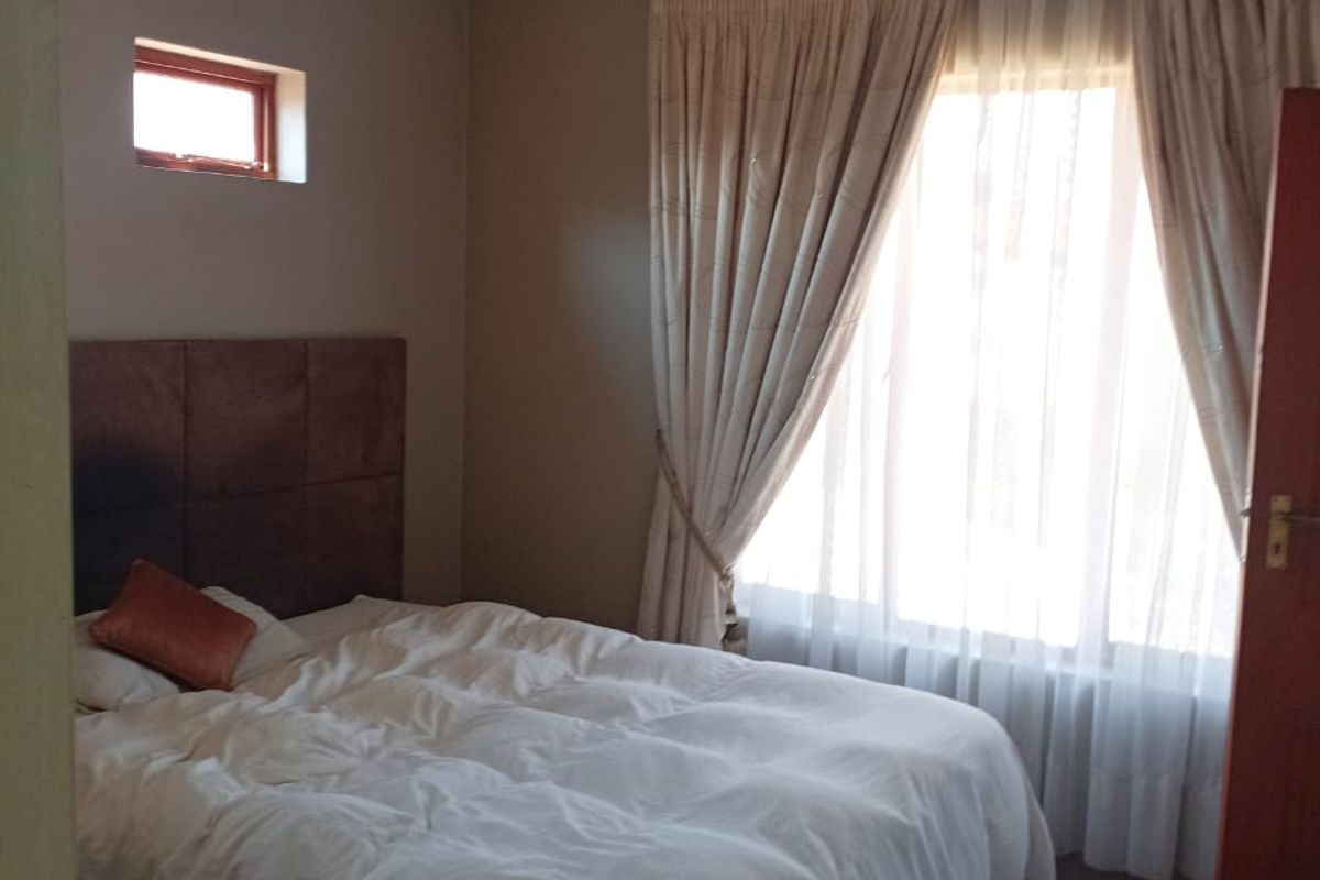 A bedroom featuring neutral wall tones, recessed ceiling lighting, and a large window with floor-to-ceiling curtains.