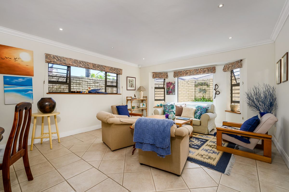 A bright living room featuring tiled flooring, recessed downlighting, and large windows with views of the exterior brick wall.