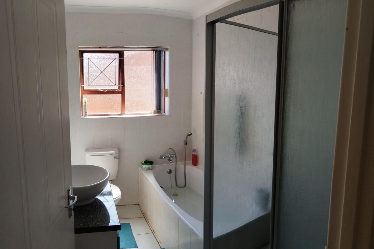 A functional bathroom featuring a built-in bathtub with shower screen, a vanity basin, and a toilet, finished with neutral wall tiles.