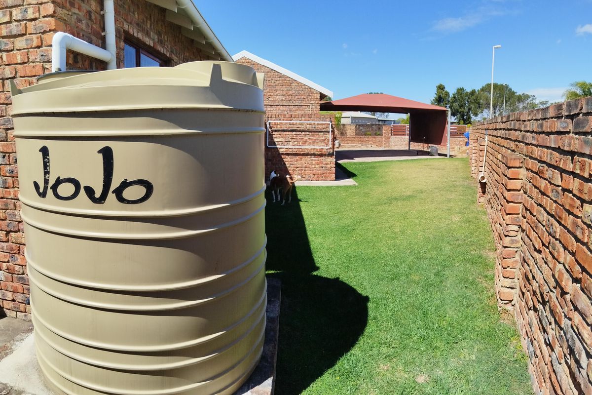 A side garden area featuring a large water storage tank, brick boundary walls, and a covered outdoor structure in the background.