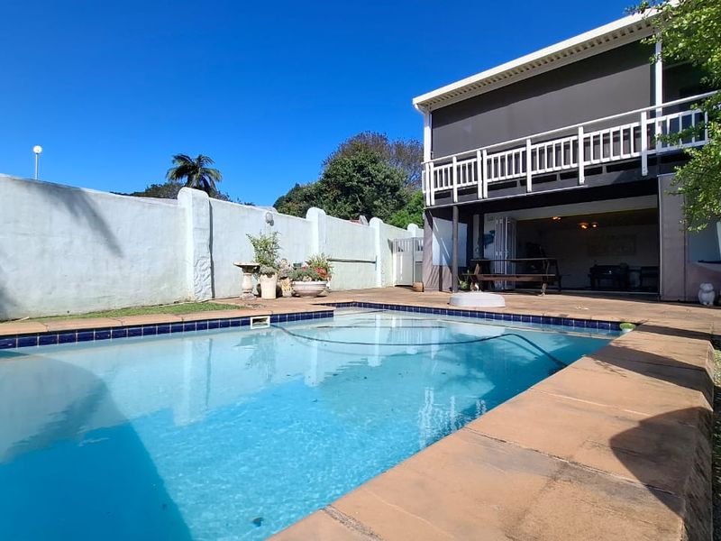 Outdoor pool area featuring a swimming pool with tiled coping, adjacent to a covered patio and a two-story dwelling with a balcony.