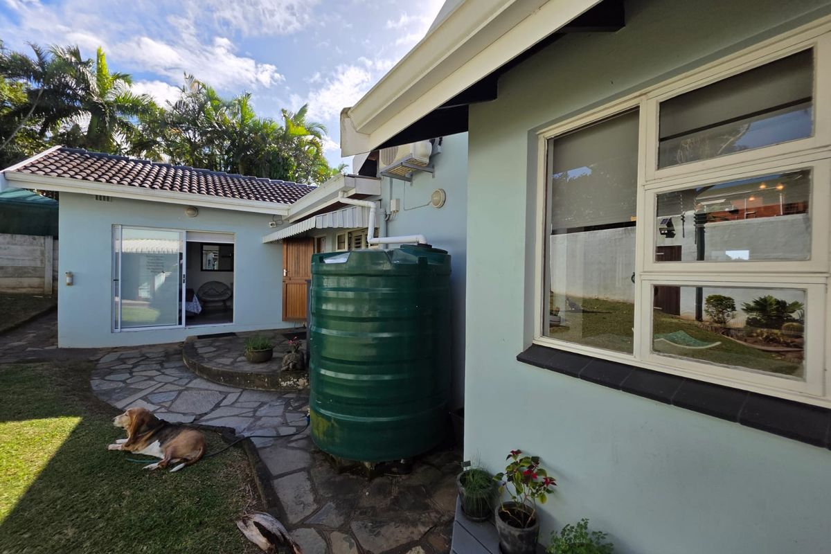 Rear exterior view of the house featuring a water storage tank, stone paved patio area, and access to the interior via a sliding door.
