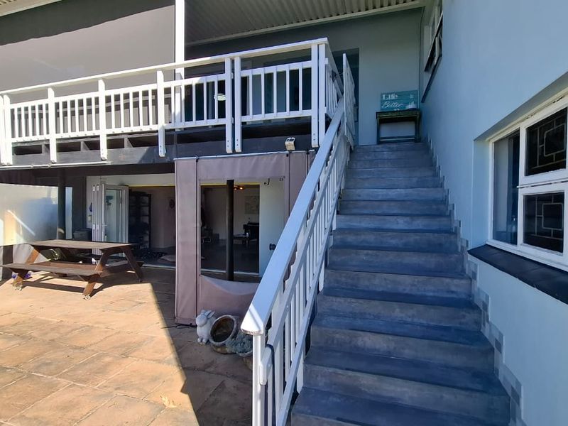 Outdoor patio area featuring a paved ground level, a raised timber deck with balustrades, and a concrete staircase leading to the upper level.