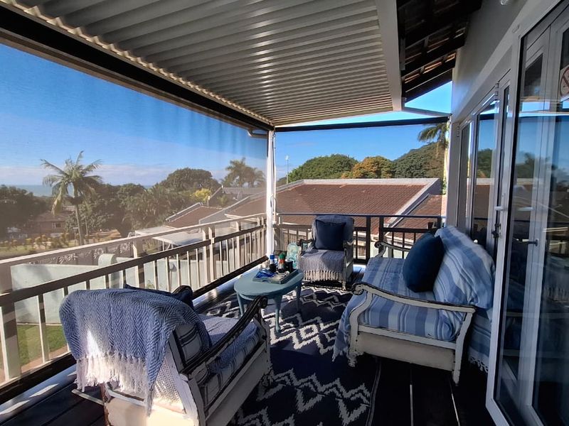 A covered balcony featuring a corrugated roof, retractable privacy screen, and sliding glass doors, offering elevated views of the surrounding landscape.