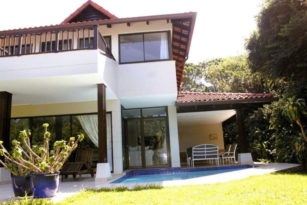 Rear view of a two-story house featuring a covered patio, swimming pool, and an upper-level balcony with dark timber accents.