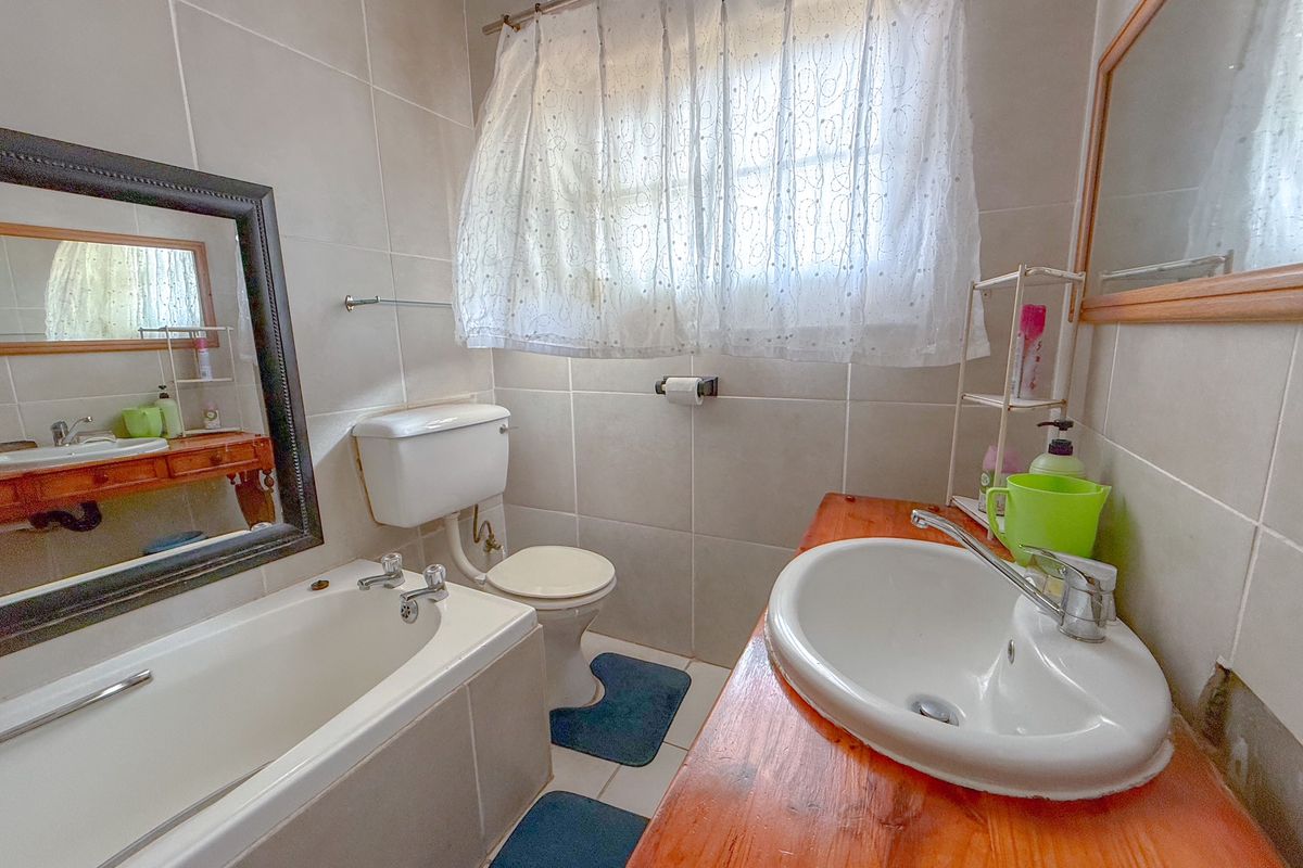 A functional bathroom featuring a built-in bathtub, a white ceramic toilet, and a timber vanity with a vessel sink.