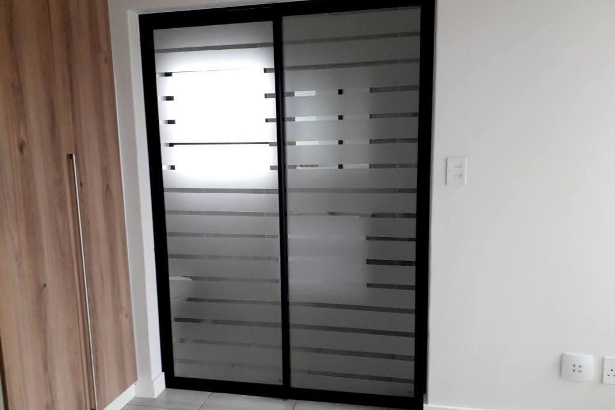 A modern interior space featuring a sleek black-framed sliding door with frosted horizontal privacy glass panels and adjacent wood-finish built-in cabinetry.