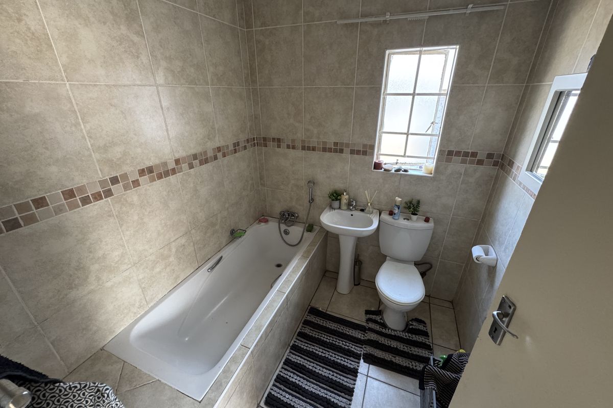 A functional bathroom featuring a built-in bathtub, pedestal basin, and toilet with neutral wall and floor tiling.