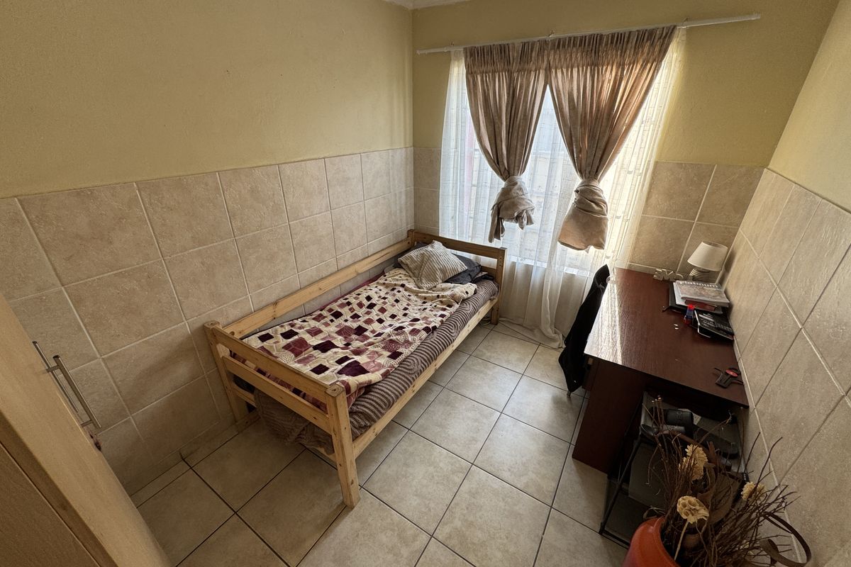 A compact bedroom featuring tiled walls and flooring, providing a functional space with natural light from the window.