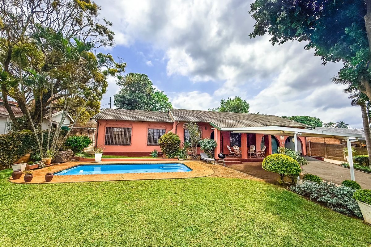 Rear view of the property featuring a swimming pool, covered patio area, and a well-maintained garden with mature trees.